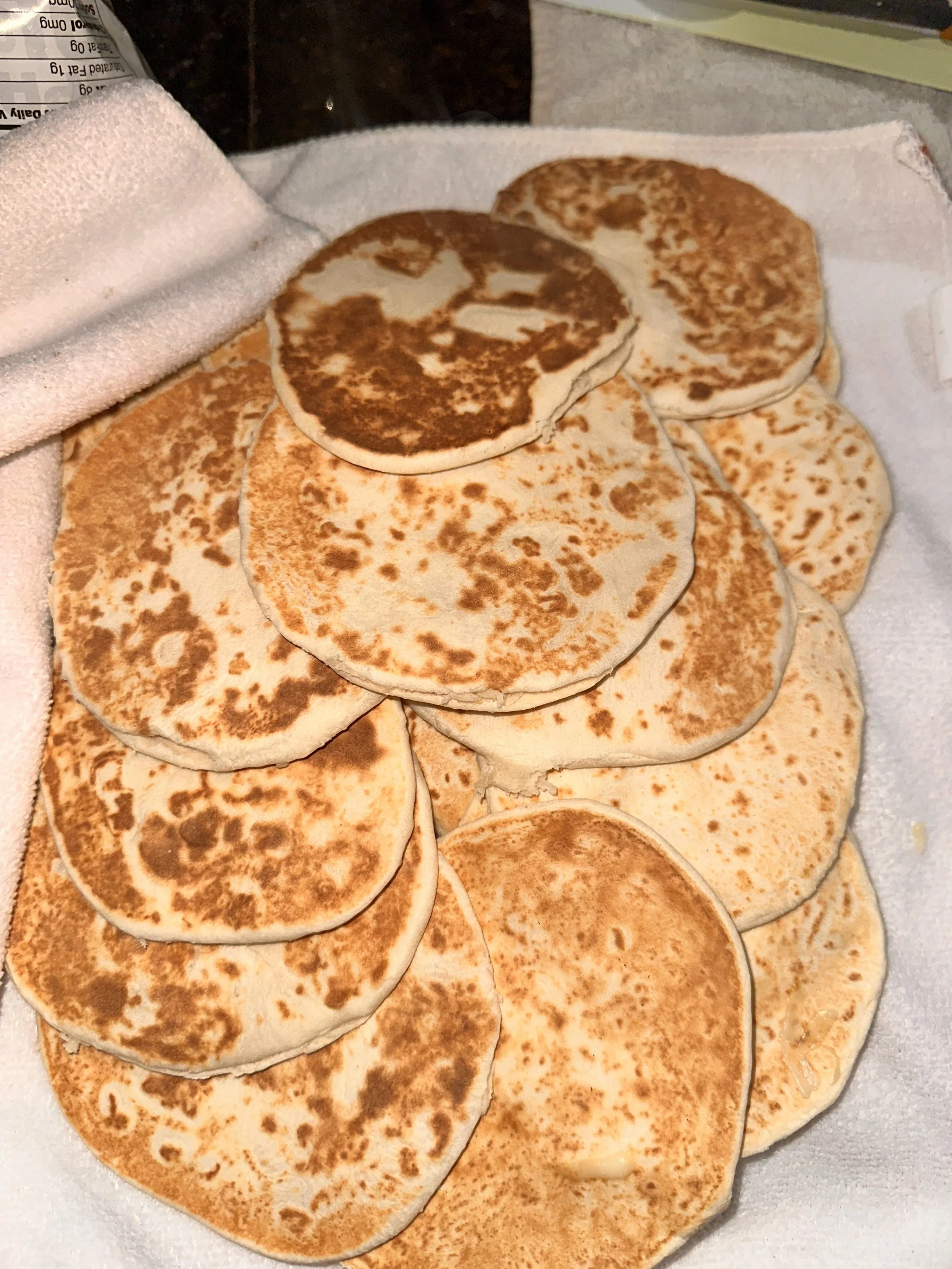 A tray of cooked pancakes, some slightly browned, stacked on a white cloth.
