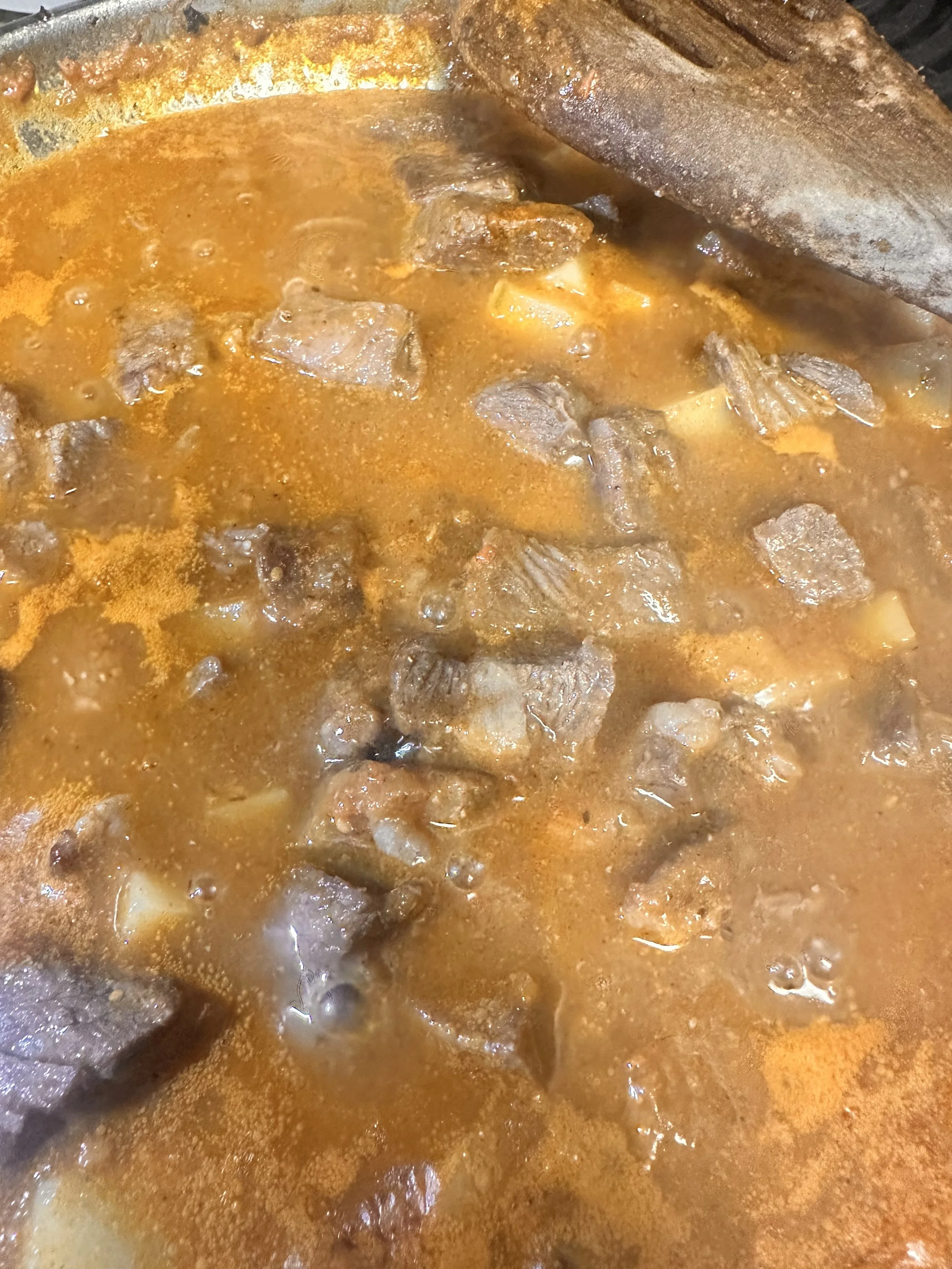 Close-up of beef stew cooking in a pot with beef chunks and a reddish broth.