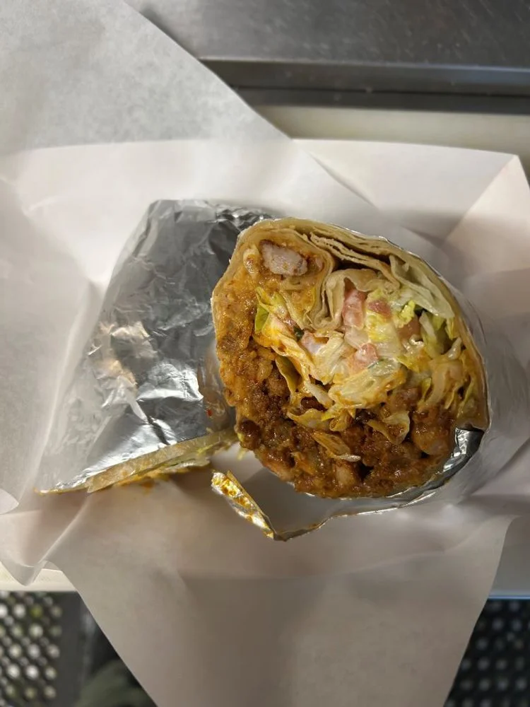 Cross-section of a burrito with meat, lettuce, and tomato inside foil wrap.