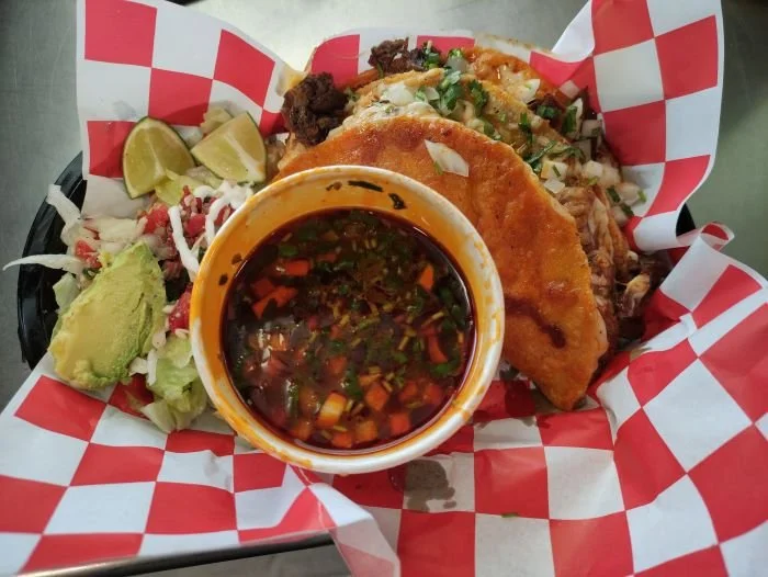 Quesabirrias lime wedges, guacamole, and a small bowl of salsa or dipping sauce.