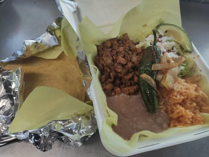 A plate with taco meat, cooked vegetables, rice, beans, and garnishes.