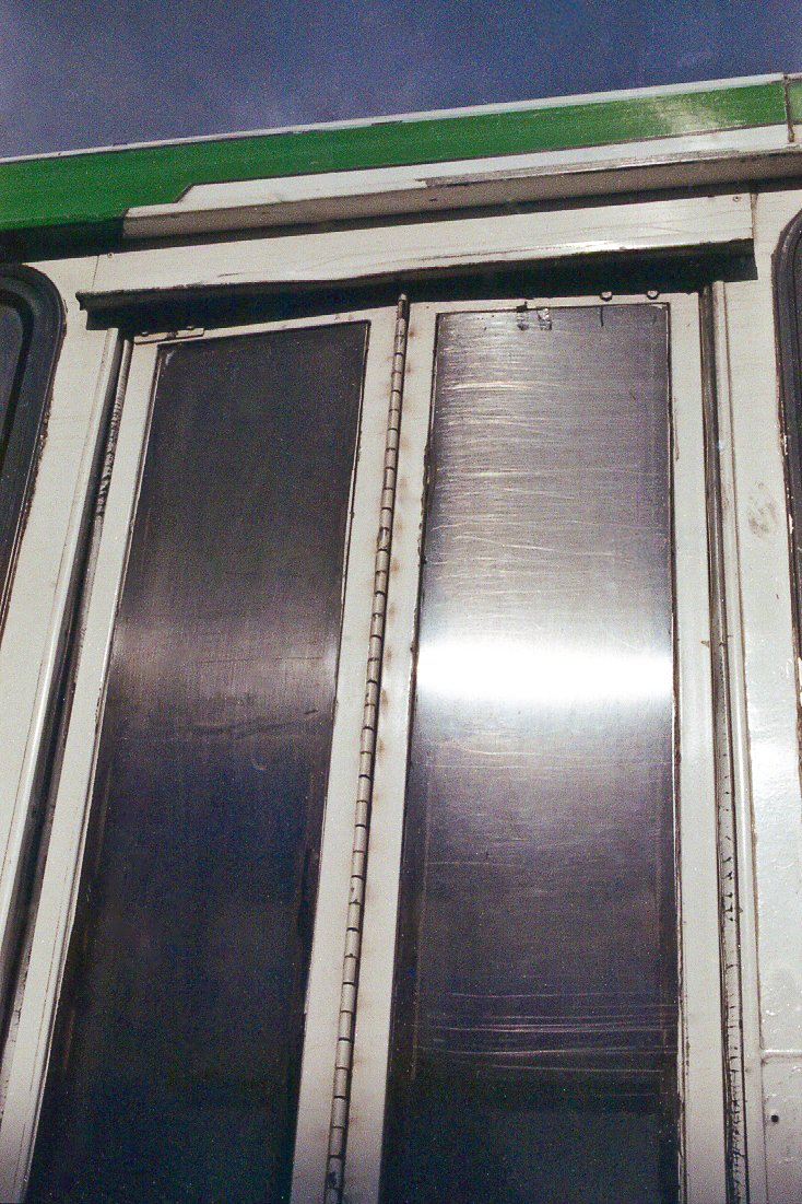 Puerta metálica con paneles rectangulares y estructura de aluminio, con un marco pintado de blanco y detalles en negro.