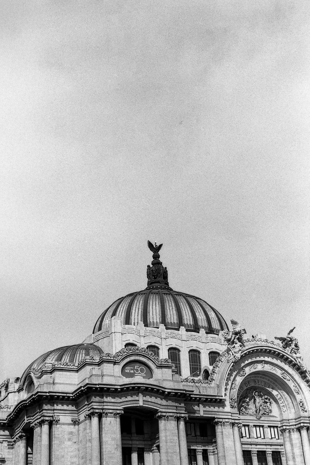 Foto en blanco y negro del techo de un edificio histórico con cúpulas y una escultura en la cúspide, con un cielo despejado de fondo.