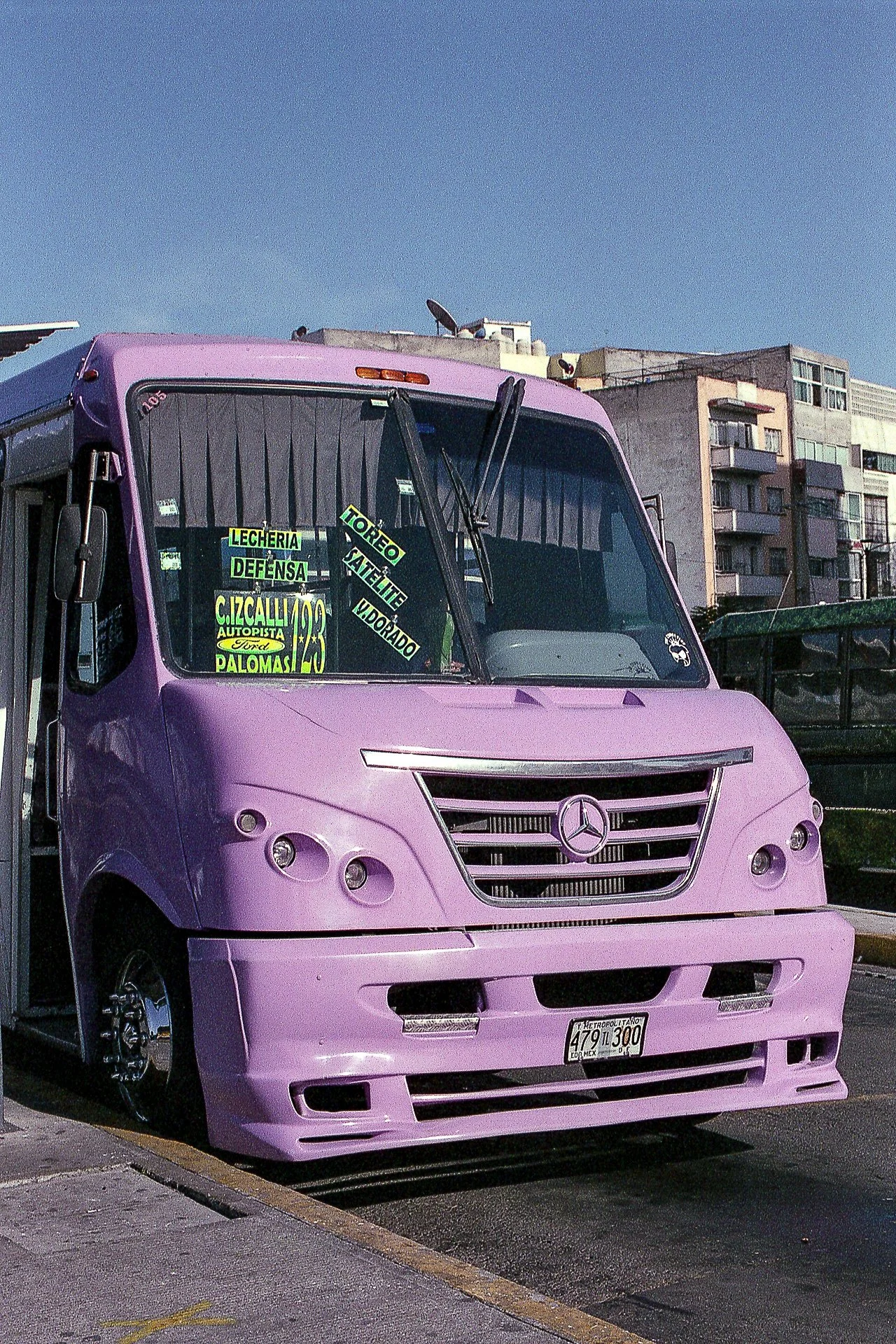 Camión rosa estacionado en la calle con publicidad en el parabrisas y edificios residenciales al fondo.
