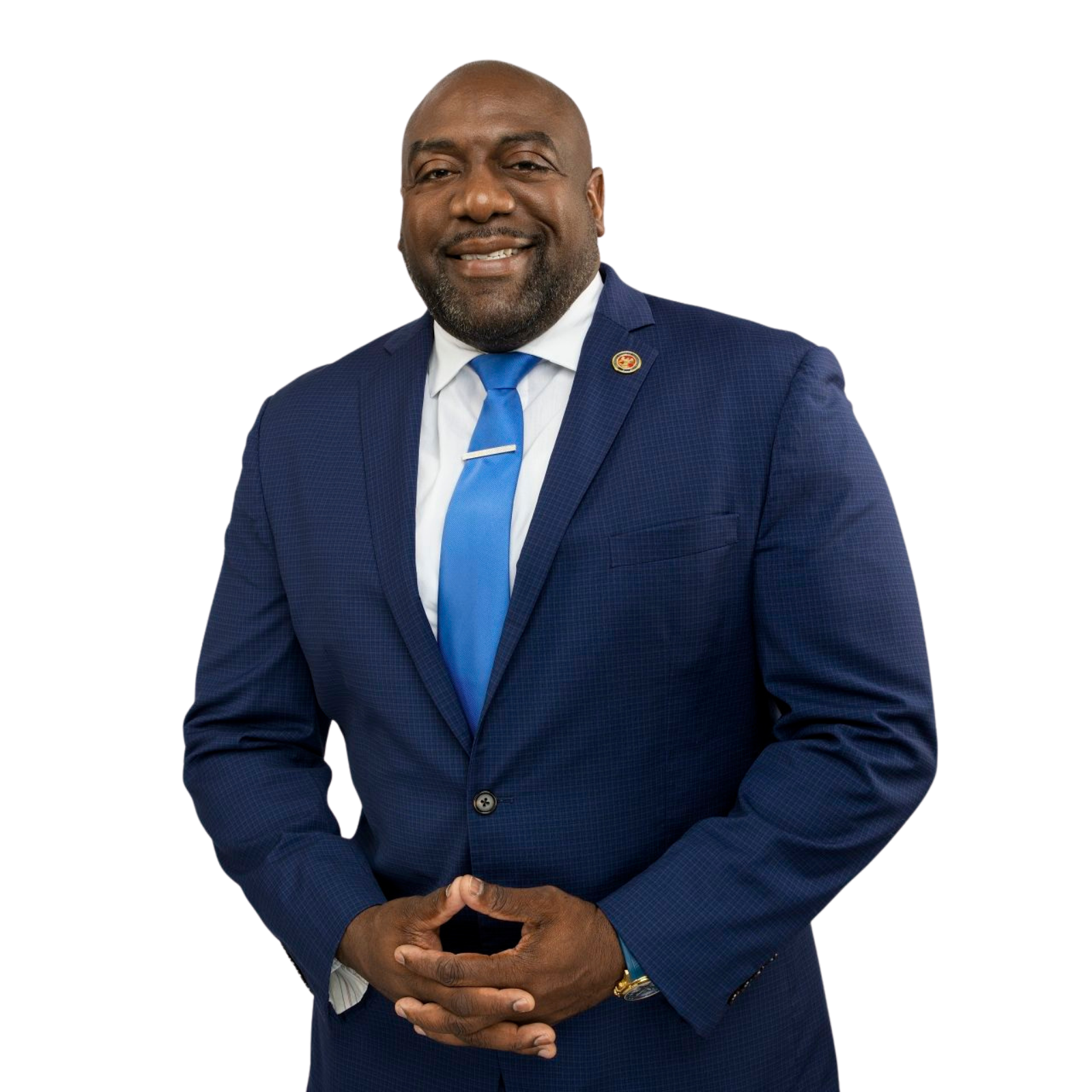 Jeffrey Hulum III in a blue business suit with a white shirt and blue tie, smiling with clasped hands, standing against a plain background.