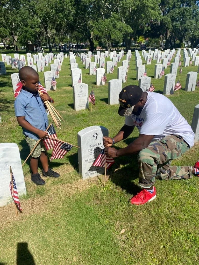 Jeffrey Hulum III and a young boy placing American flags at a military cemetery headstone on Memorial Day.