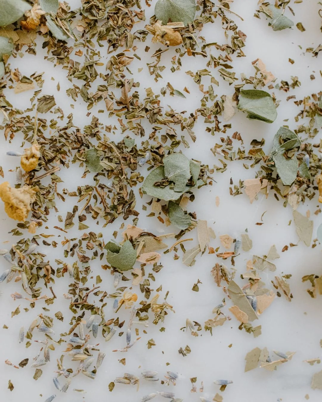 Dried herbs and leaves scattered on a white surface.