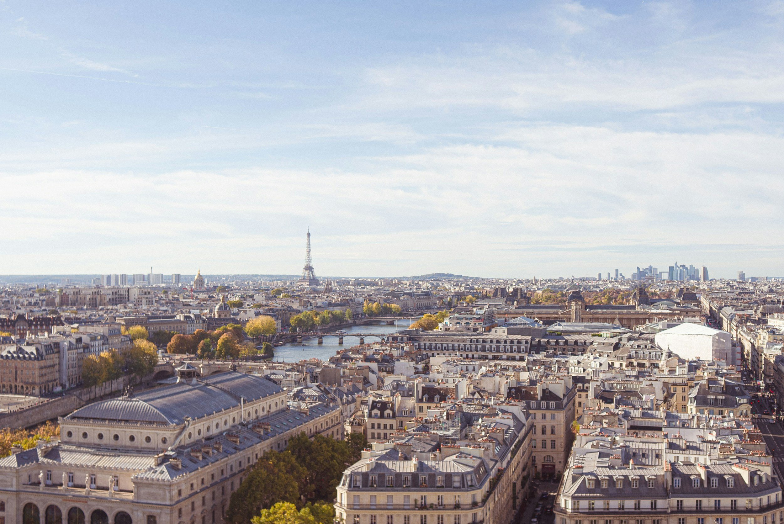 Vue panoramique de Paris avec la tour Eiffel, la Seine, et des bâtiments historiques sous un ciel partiellement couvert.