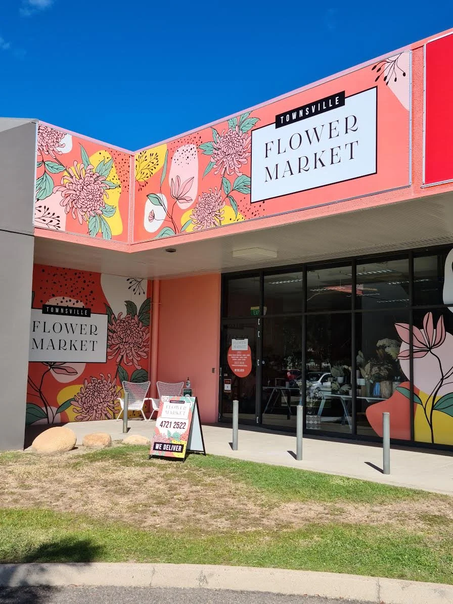 Exterior of a Florist with pink and floral artwork on the walls and signage, outdoor seating, and a sidewalk in front.