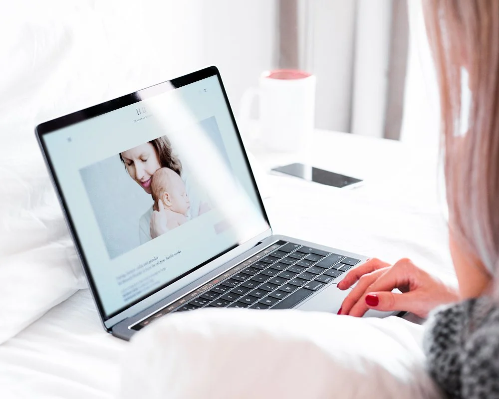 Person with red nail polish browsing a webpage on a laptop, displaying a photo of a woman holding a baby.