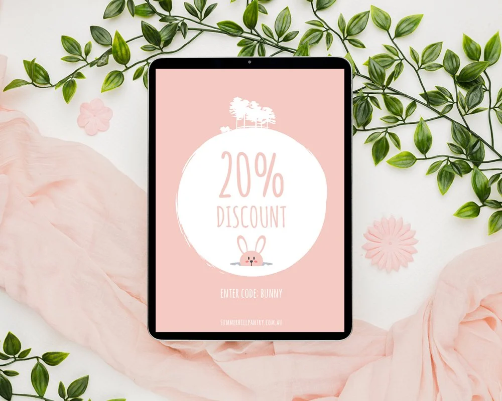 Tablet displaying a promotional offer of 20% discount with a bunny illustration. The background includes pink fabric, green leaves, and pink flowers.