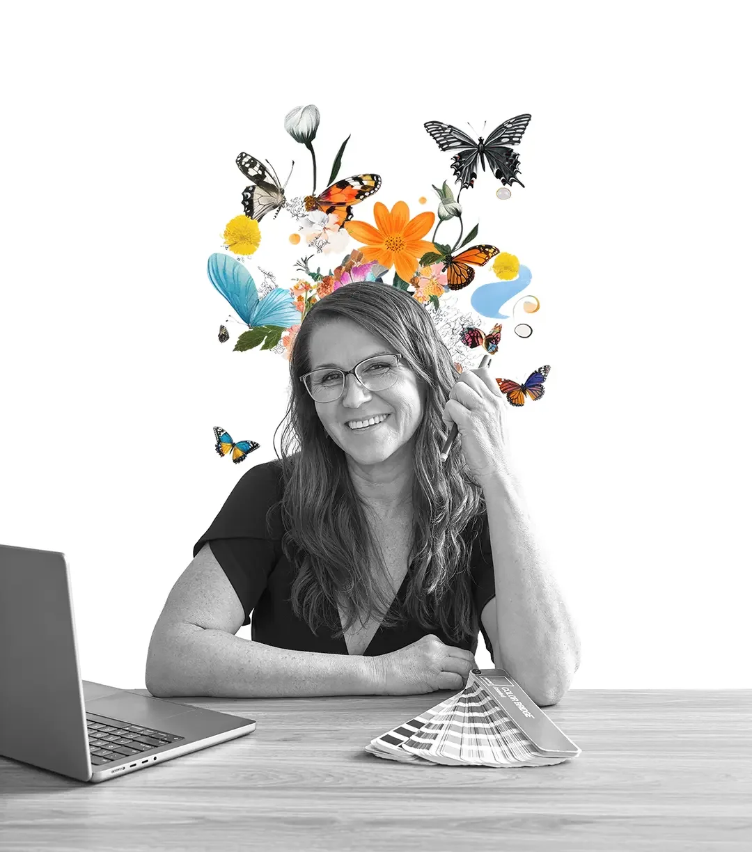 A woman smiling with long hair and glasses sitting at a desk with a laptop and color swatches, with colorful butterflies and flowers digitally illustrated above her head.