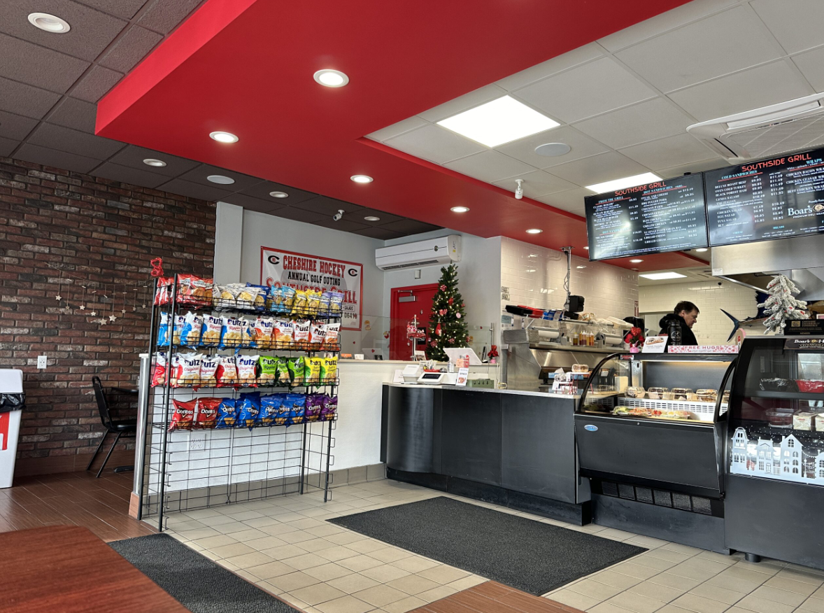 Interior of a fast food restaurant with a counter, digital menu boards, a Christmas tree, and snack rack.