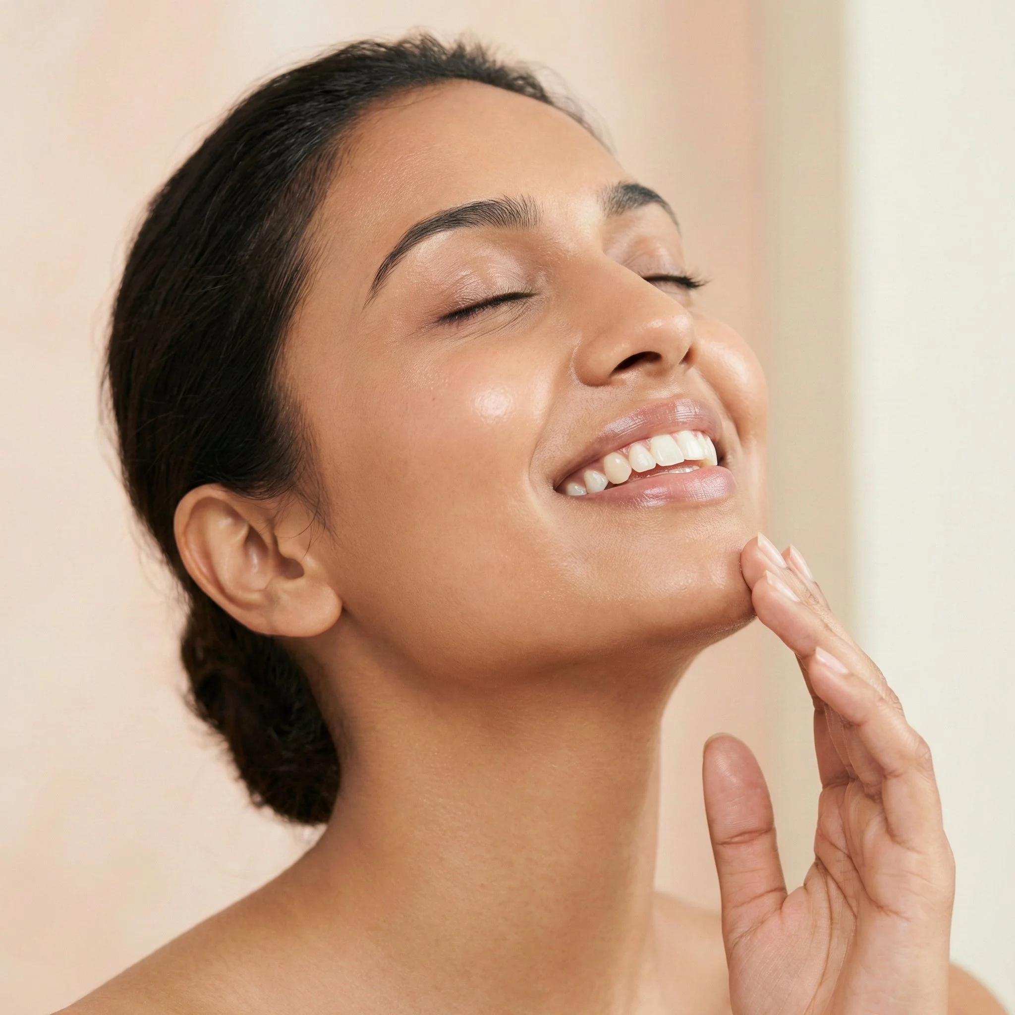 Close-up of a smiling woman with her eyes closed, touching her chin with her fingers.