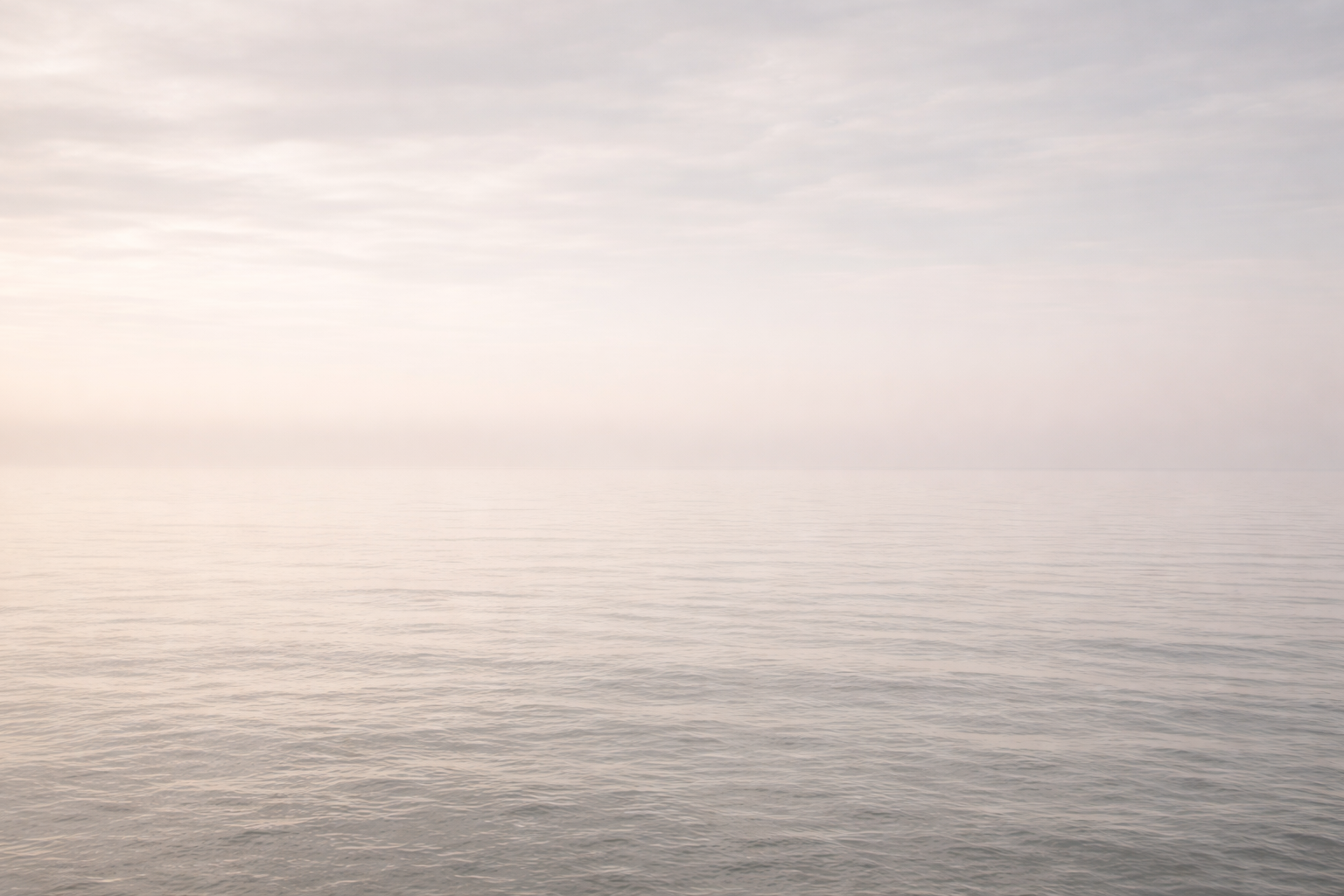 Calm ocean waters with a misty, overcast sky and soft pastel colors.