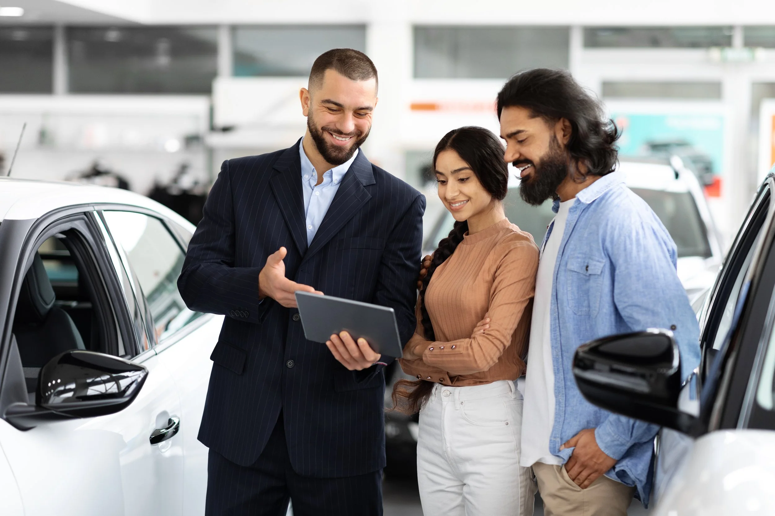 A car salesman showing a tablet to a couple at a car dealership.