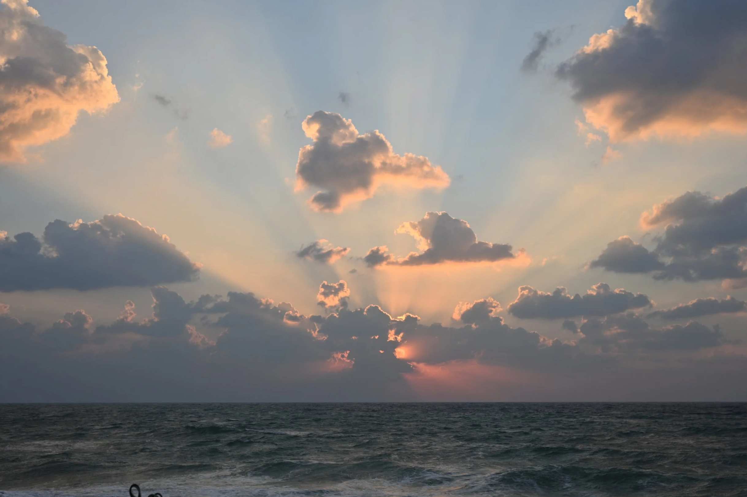 Sunset over the ocean with clouds and rays of sunlight breaking through.