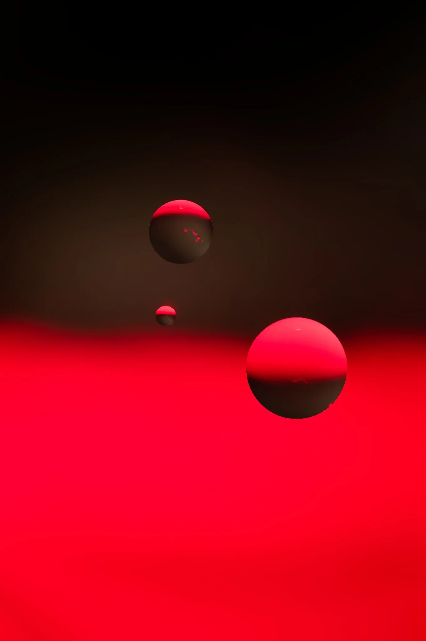 Abstract digital artwork featuring three spheres floating in a dark space with red and black color gradient background.