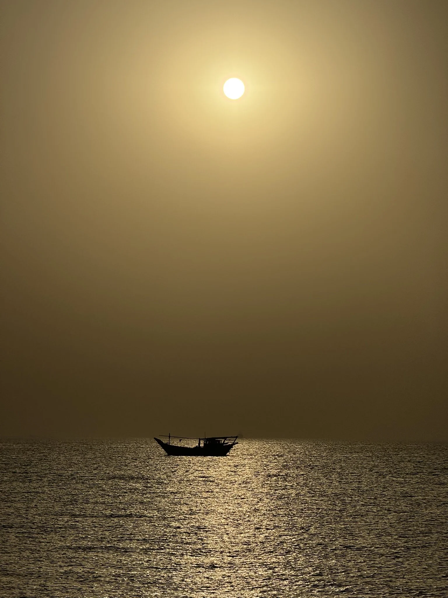 A boat floating on the water during a sunset or sunrise with the sun high in the sky.