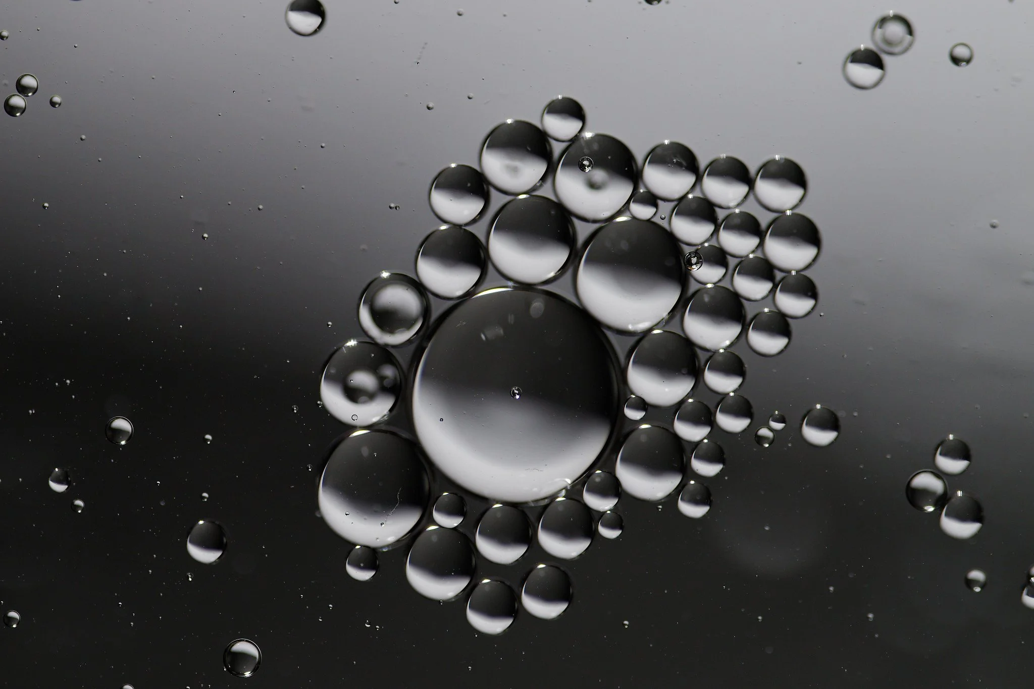 Close-up of oil droplets on water, showing various sizes of round bubbles against a dark background.