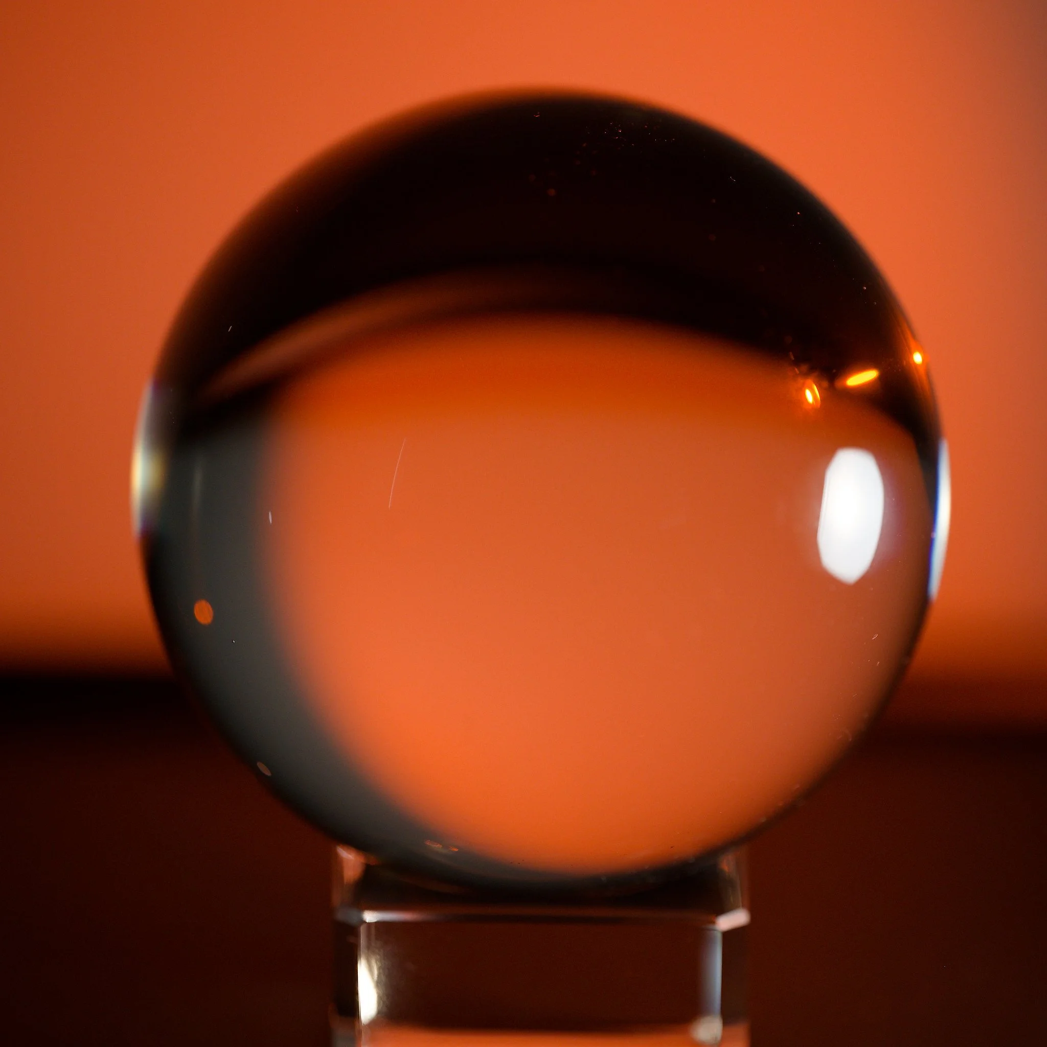 Close-up of a glass sphere with a warm orange background, reflecting light and creating a smooth, glossy surface.