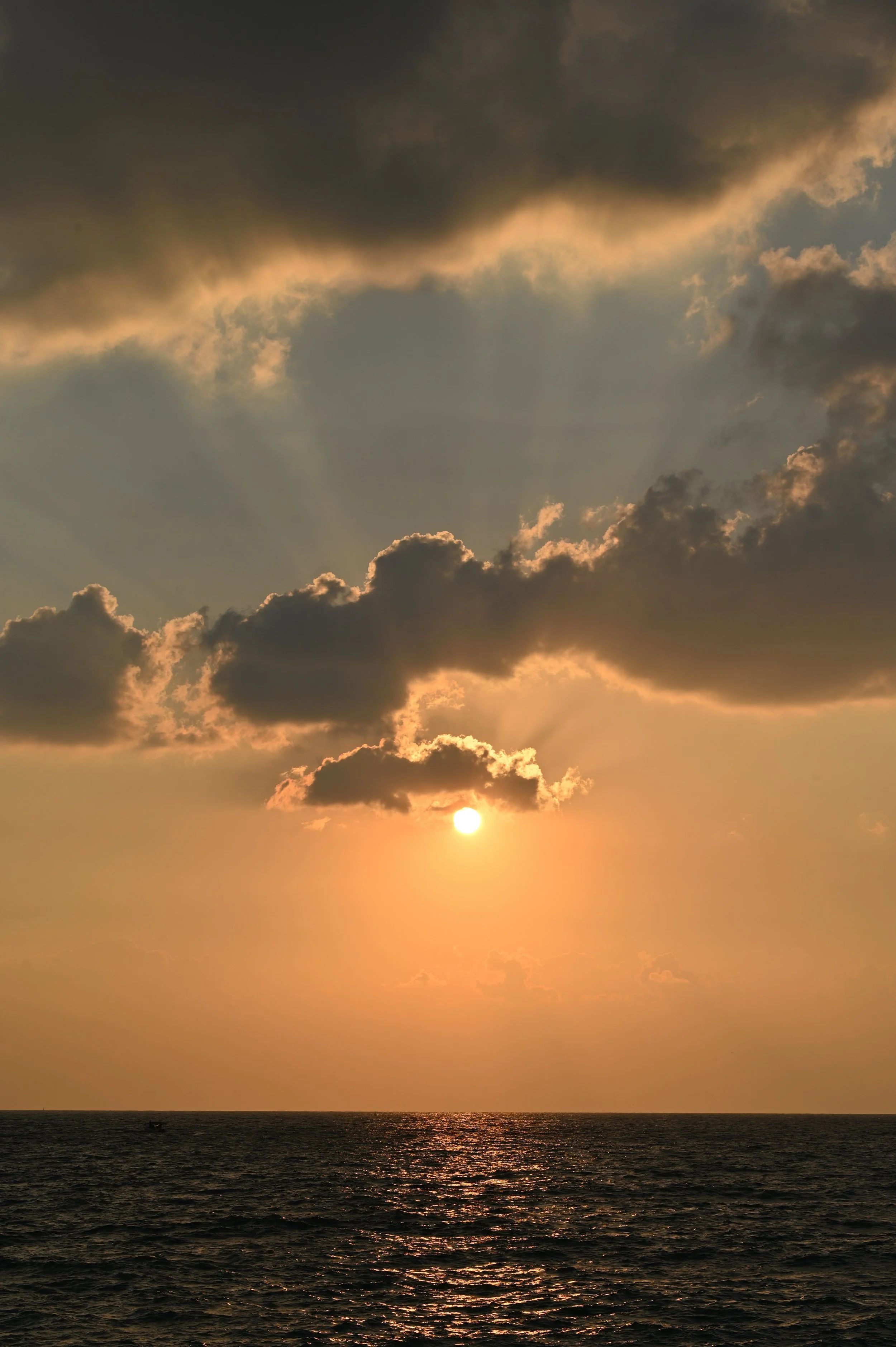 Sunset over the ocean with partly cloudy skies and sun rays streaming through clouds.