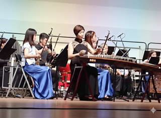 Wan Chun Shui, a Taiwanese guzheng legend, performing on stage with orchestra members, playing the traditional instruments