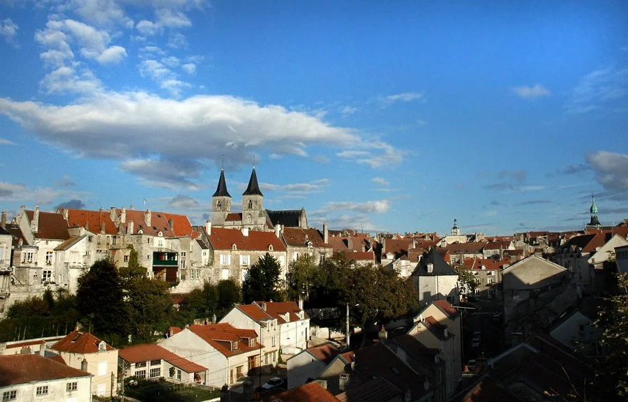 Panoramic view of a European city with traditional buildings, two prominent church steeples, and a blue sky with clouds.