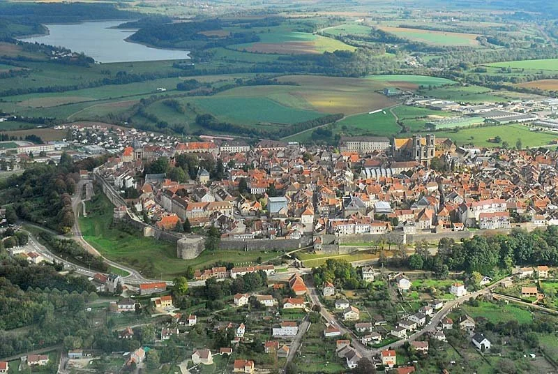Aerial view of a small town with a historic castle and church, surrounded by farmland and a lake in the background.