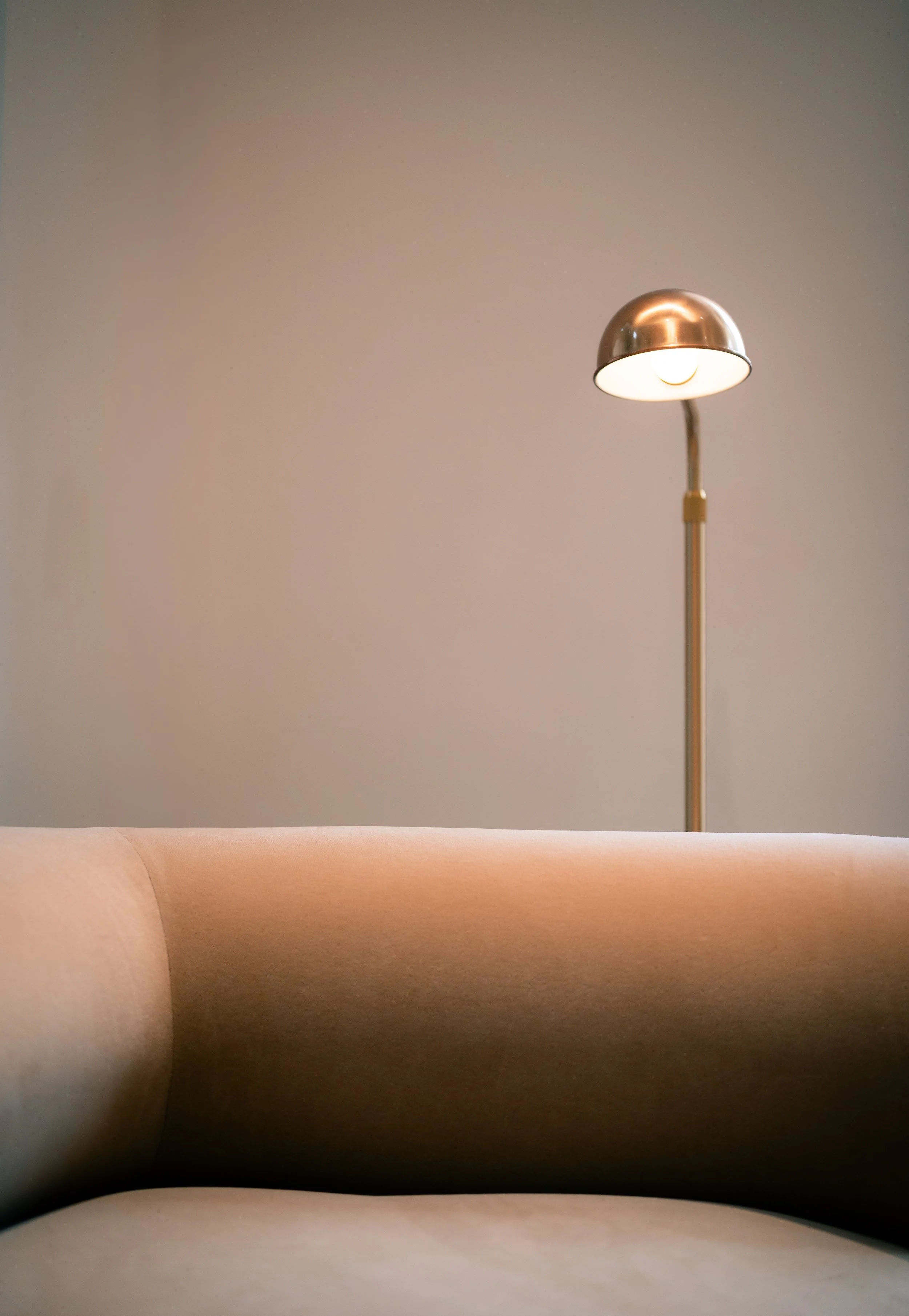 A minimalist room with a beige sofa and a modern floor lamp with a metallic shade against a plain wall.