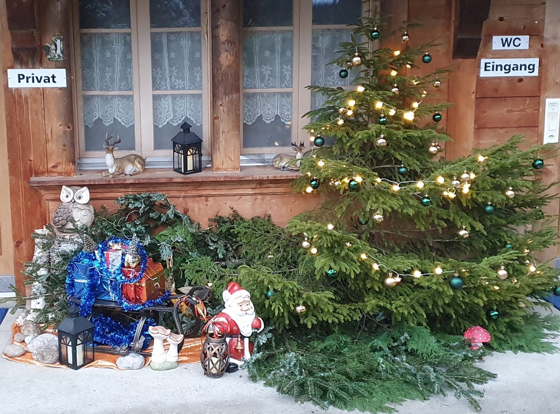 Weihnachtsdekoration mit Tannenbaum, Christbaumkugeln, Lichterkette, Weihnachtsfiguren, Schneeflocken, und dekorativen Tieren an einem Holzhaus