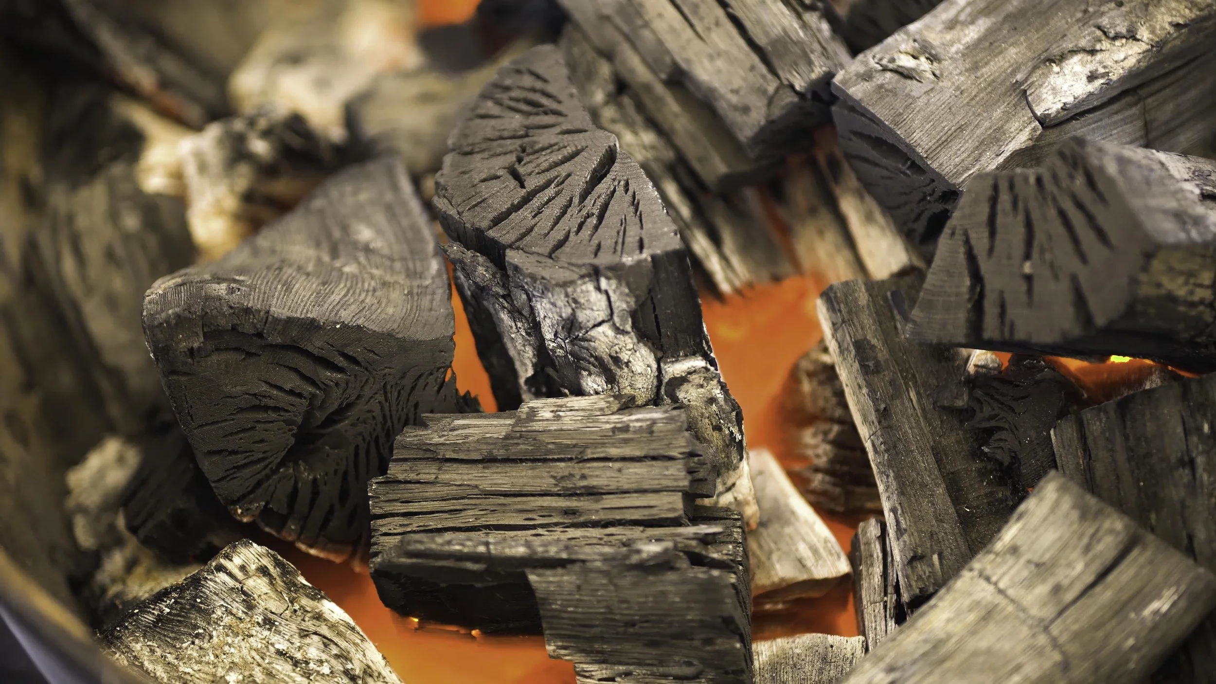 Close-up of burning charcoal pieces with visible cracks and wood grain patterns, glowing orange embers underneath.