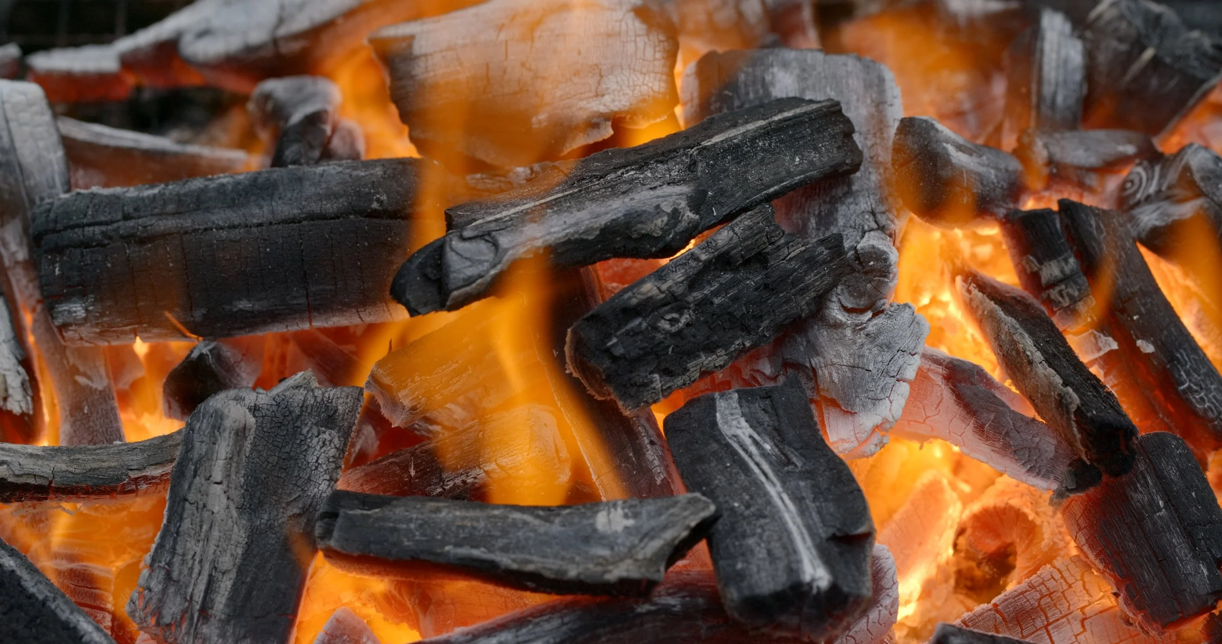 Close-up of burning charcoal with glowing orange embers and blackened logs.