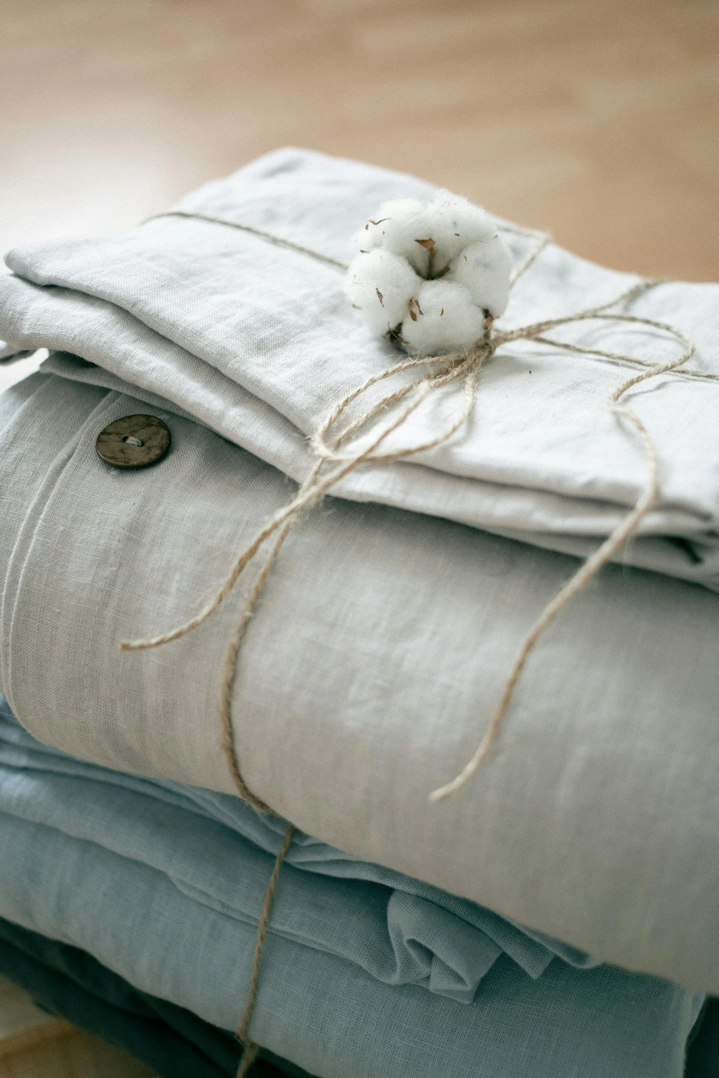 Stacked folded light-colored linen and cotton fabric with a cotton stem tied with twine on top.