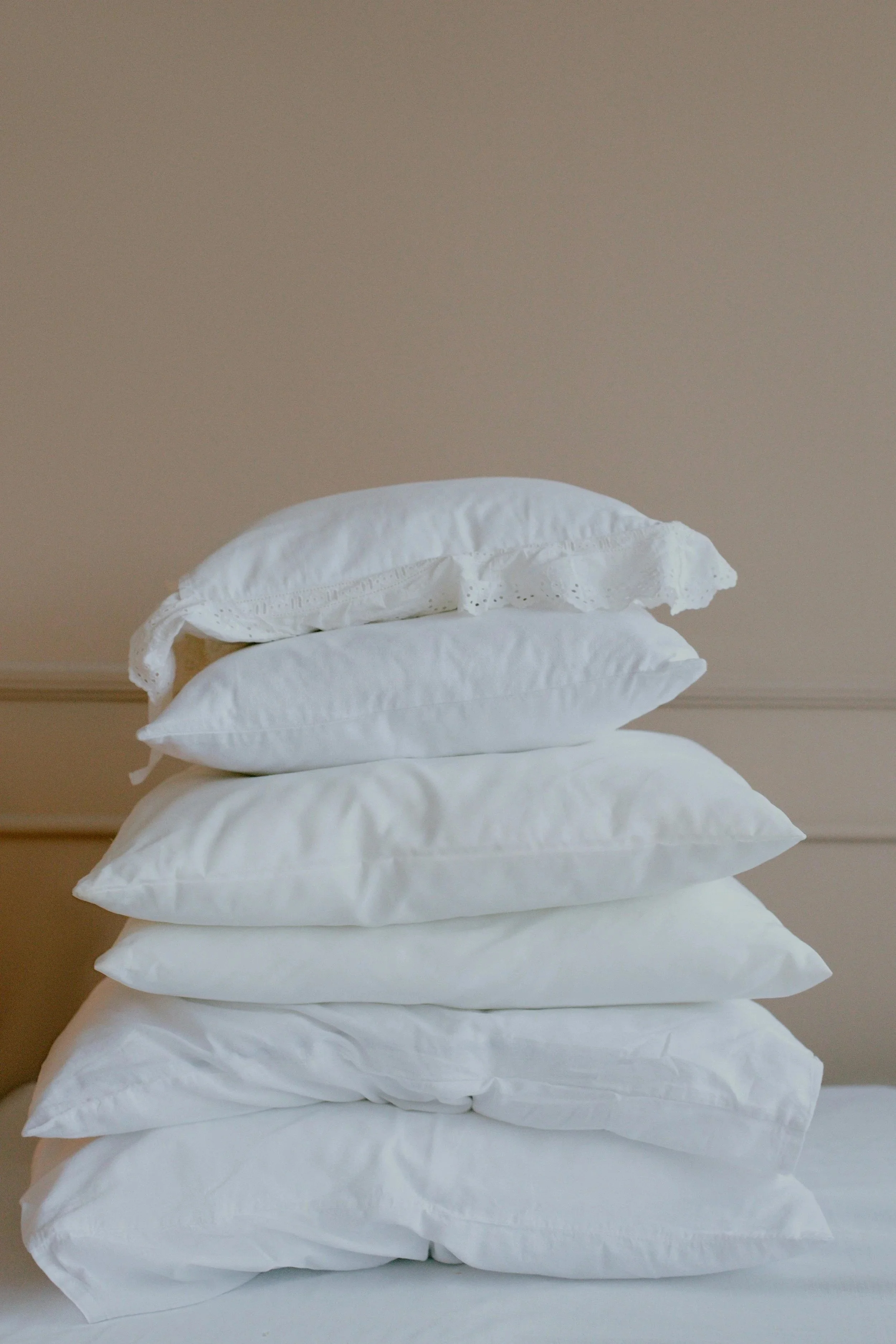 Stack of eight white pillows on a bed against a beige wall.
