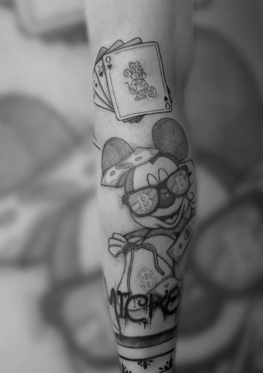 Tattoo von Mickey mouse  mit Sonnenbrille, die mit Bitcoin-Symbolen bedeckt ist, und einem Kartenspiel (König, Dame, Bube, Ass) auf einem Unterarm.