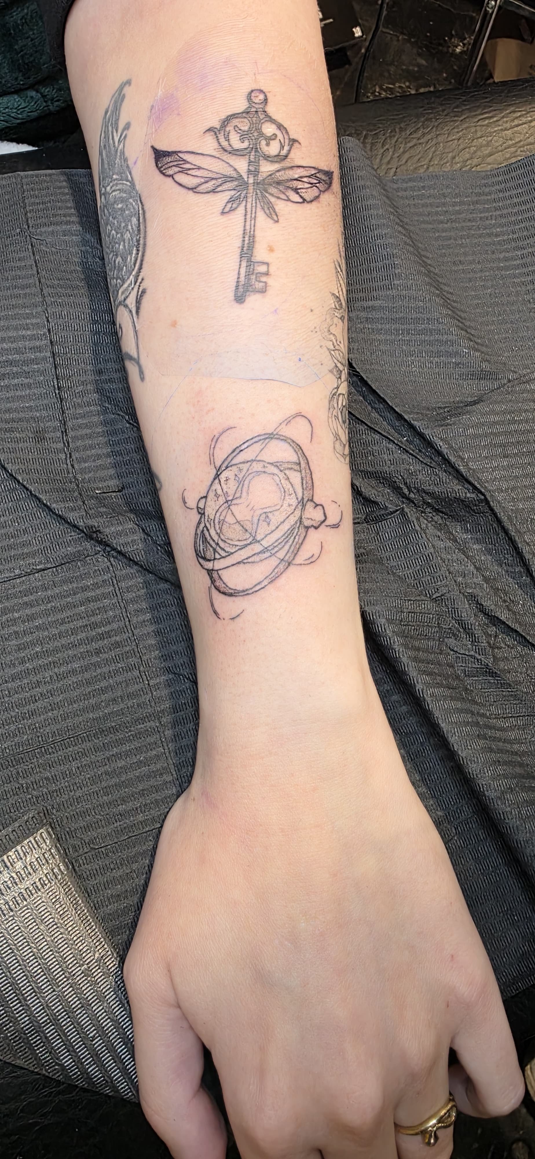 Tattoo auf dem Unterarm mit einer antiken Schlüssel, einer Fliege und einem Planeten