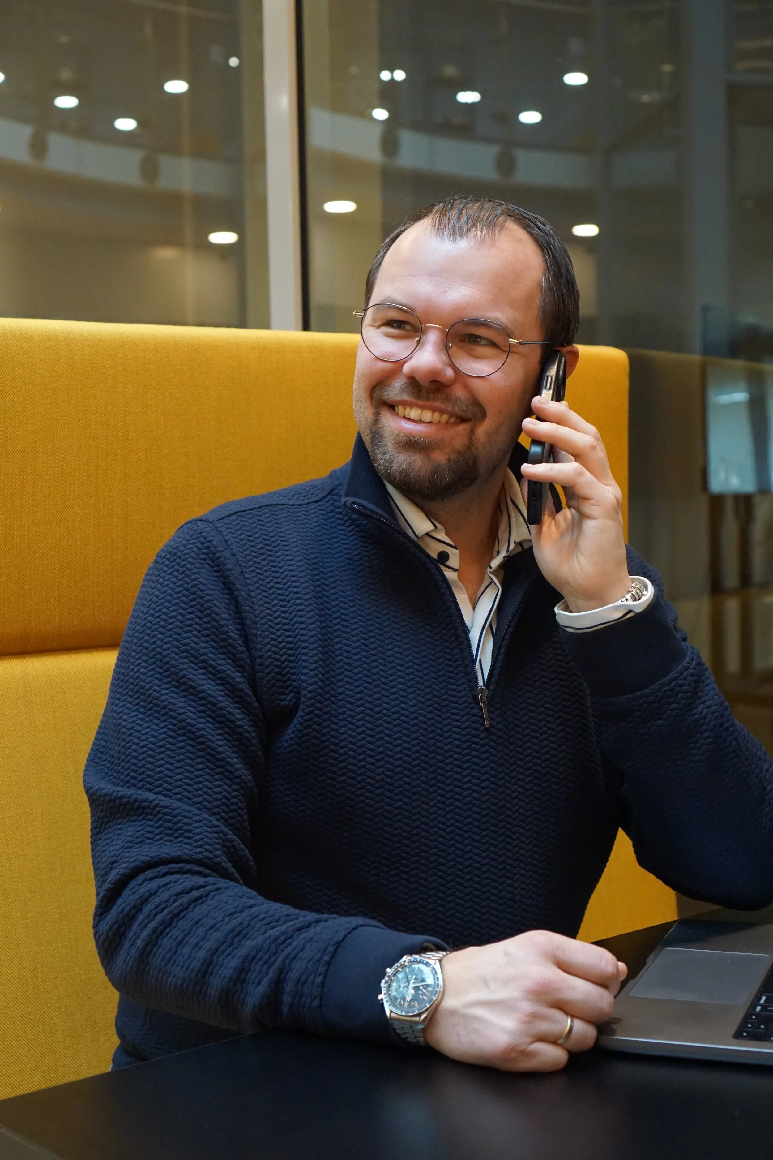 Man die op een laptop werkt en die telefoon in de hand houdt in een moderne kantooromgeving. Neem contact op met Rethink.