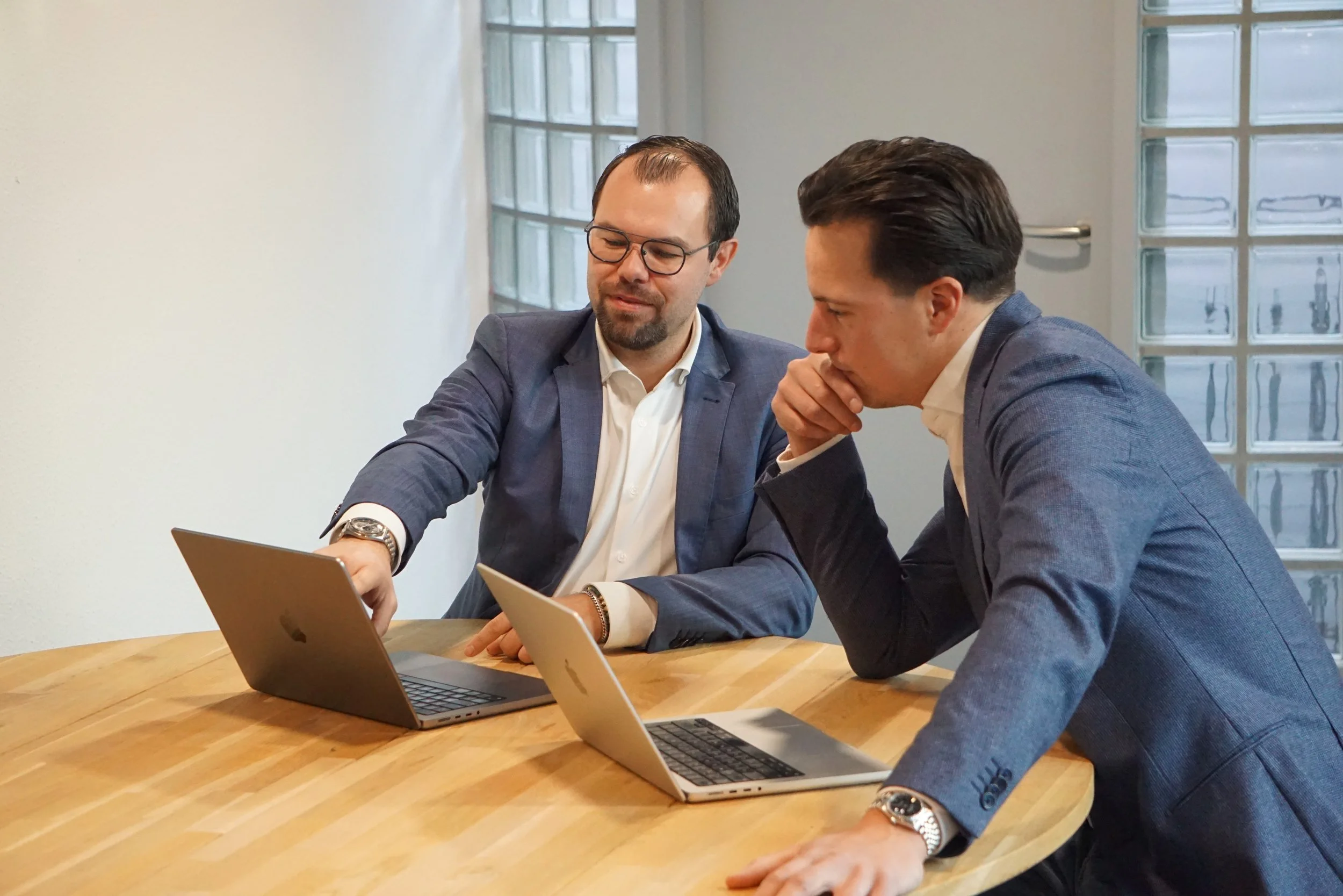 Twee zakenmensen in een bespreking met laptops aan een houten tafel in een vergaderruimte.