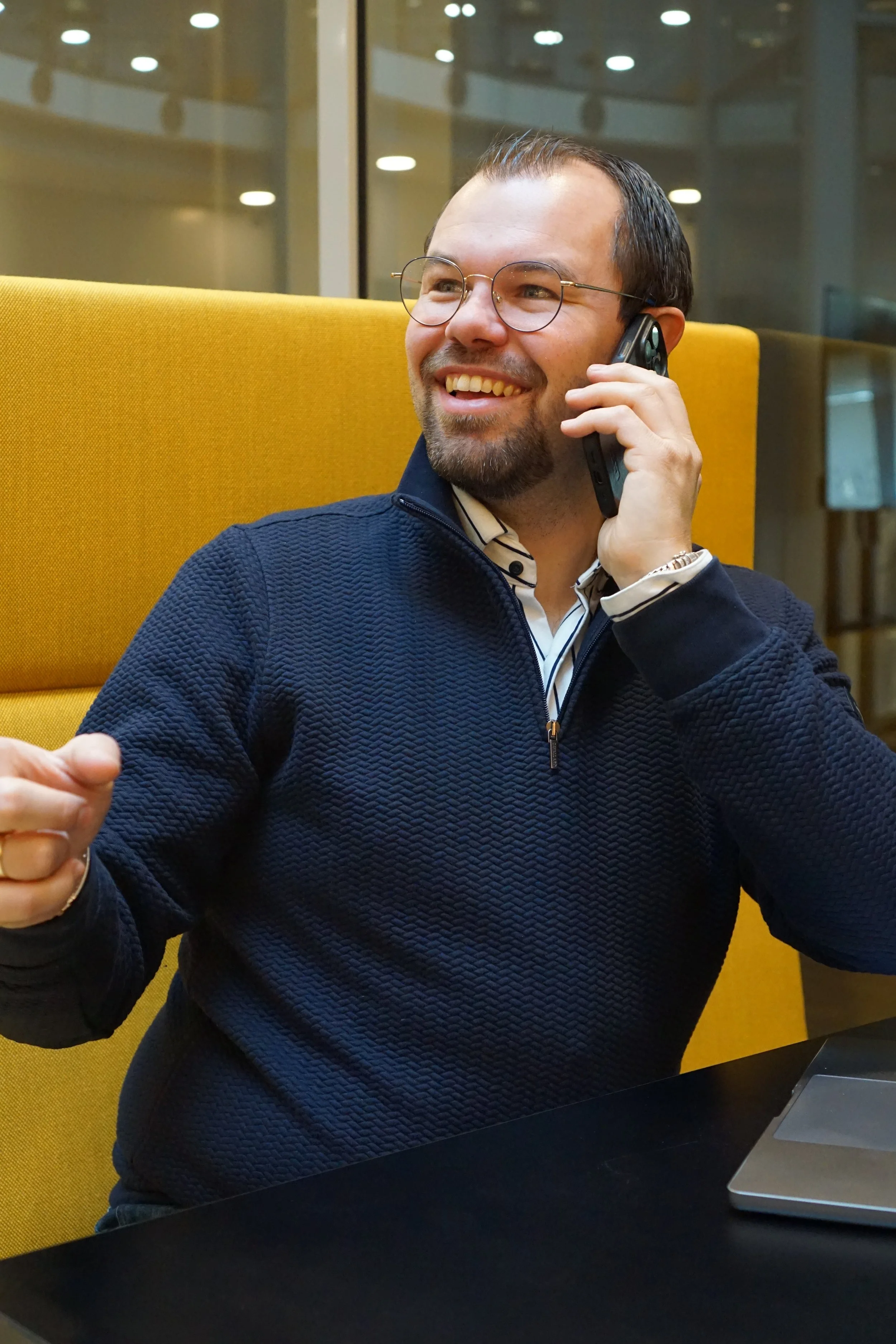 Man die op een laptop werkt en die telefoon in de hand houdt in een moderne kantooromgeving. Neem contact op met Rethink.