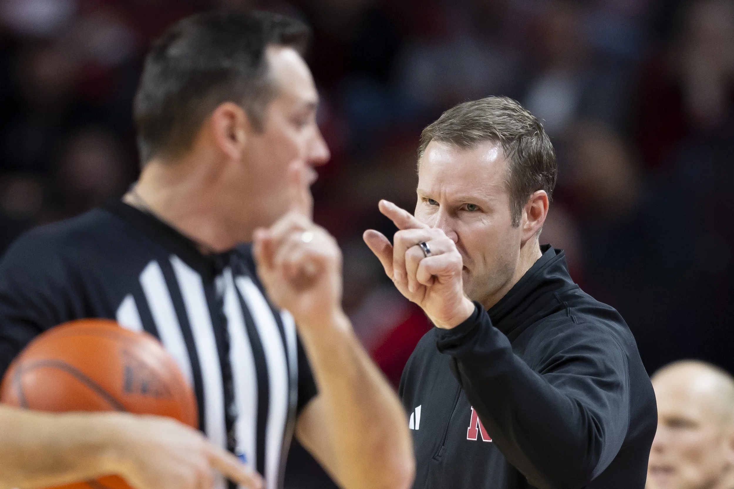 A basketball referee with a basketball in hand listening to a coach during a game, gesturing with his finger.