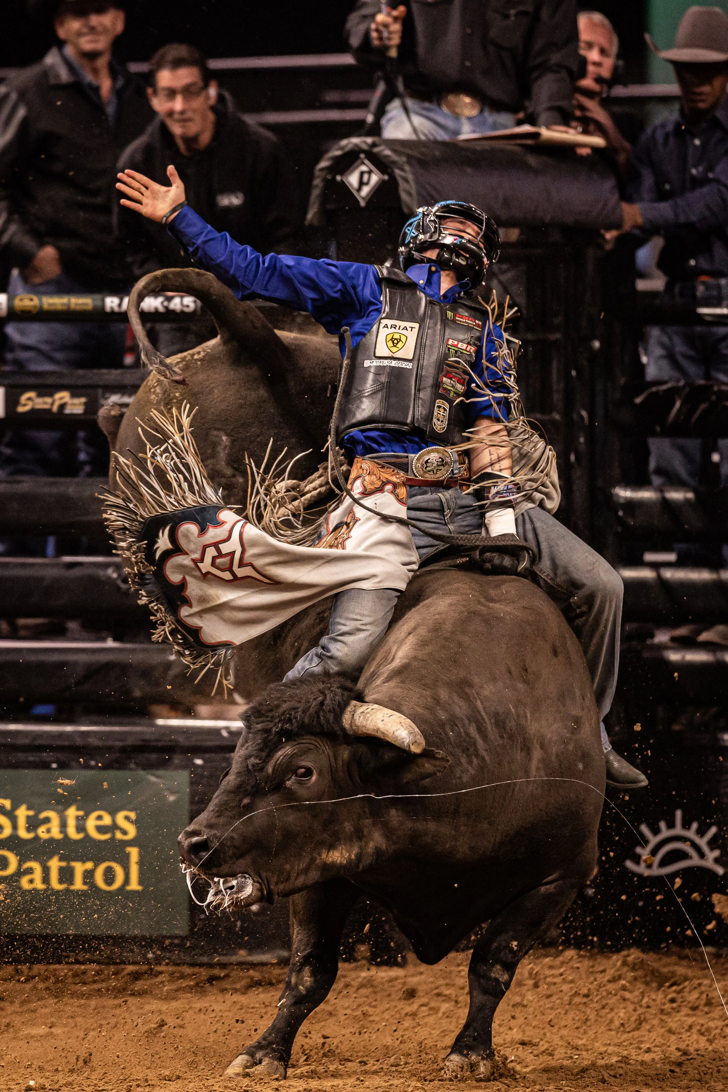 A rodeo rider on a bull inside an arena, with spectators watching in the background.