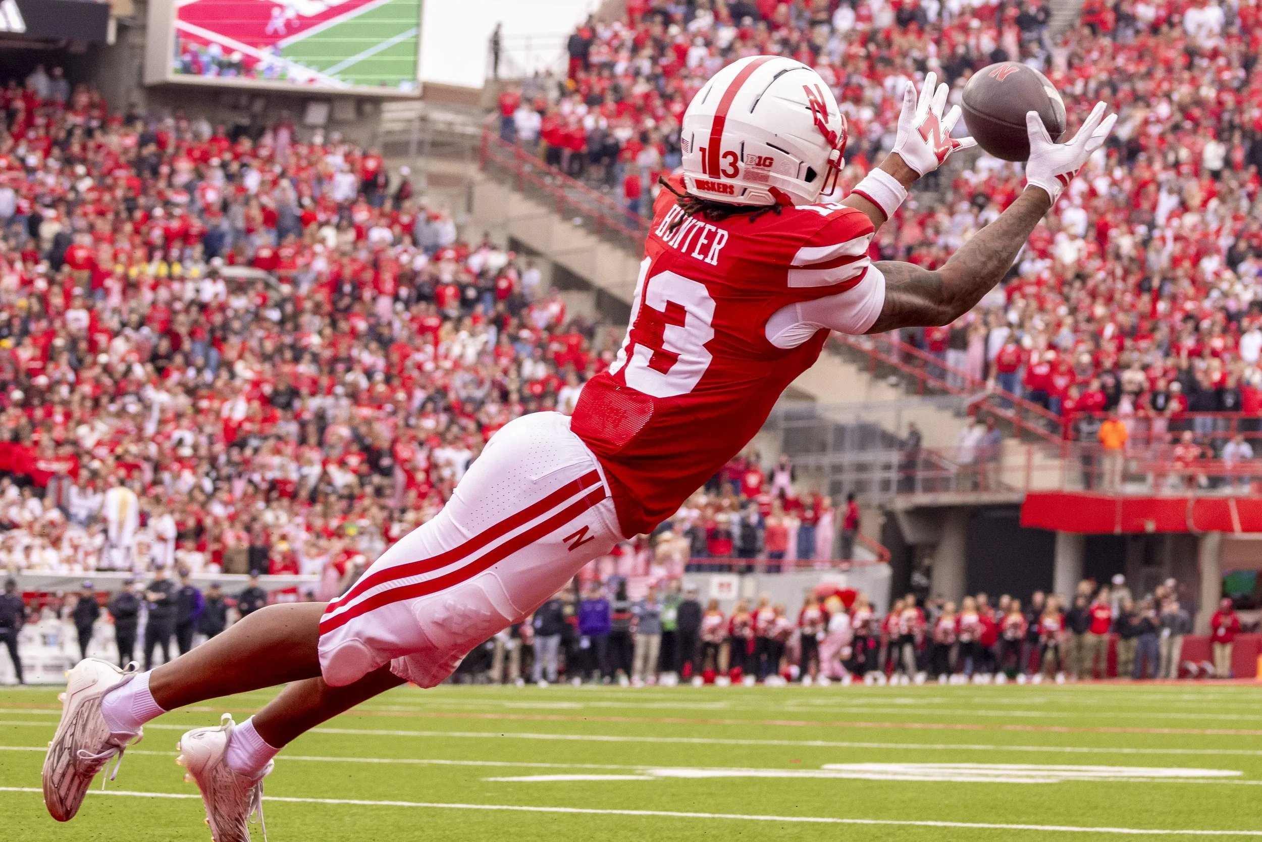 An American football player in a red uniform catching a football during a game in a large stadium full of fans.
