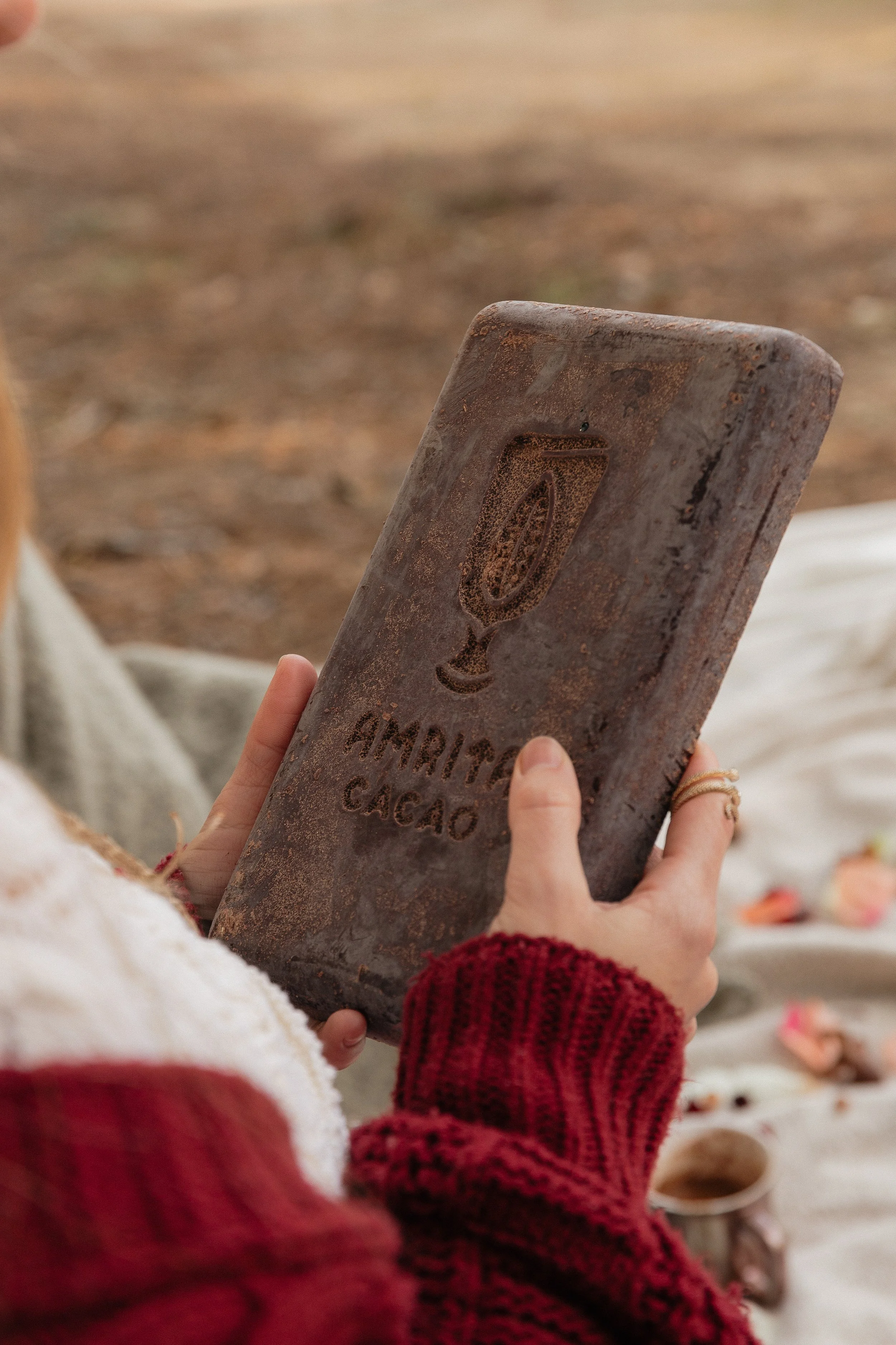 A person wearing a red and white sweater is holding a rusty metal clipboard with the word "Chicago" and an engraving of a drink glass. The background appears to be an outdoor setting with a blurred earthy ground.