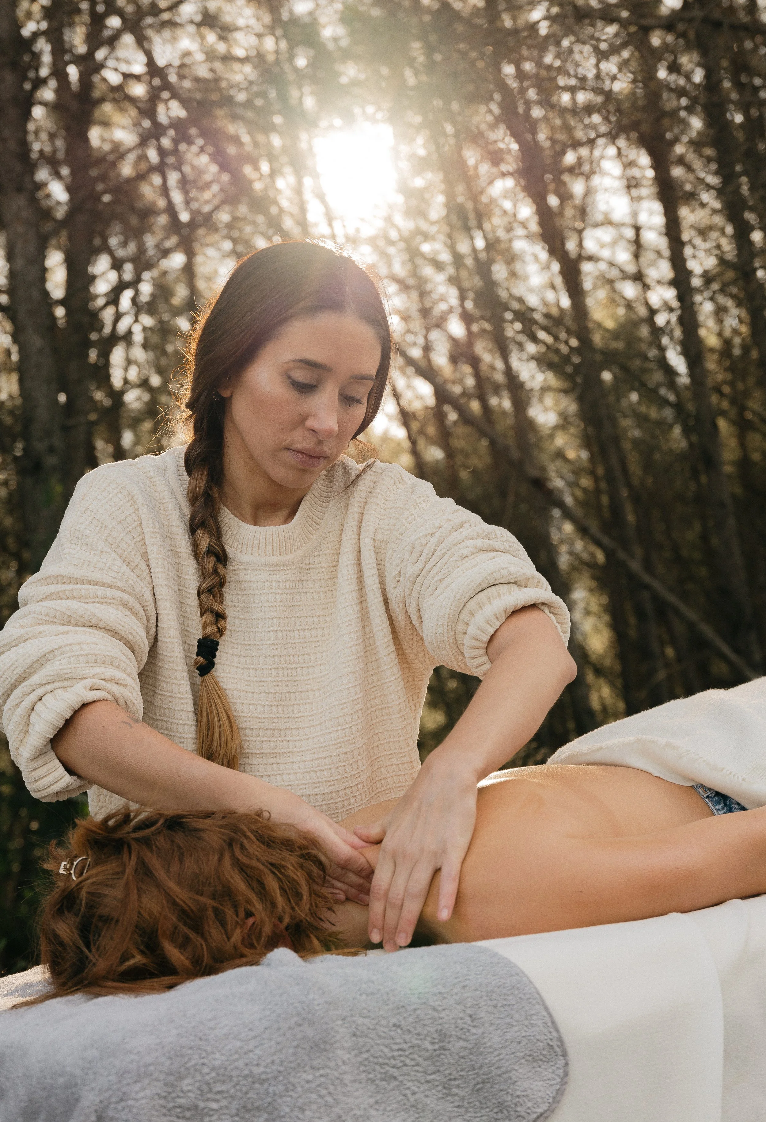 A woman giving a back massage outdoors during sunset, with trees in the background.