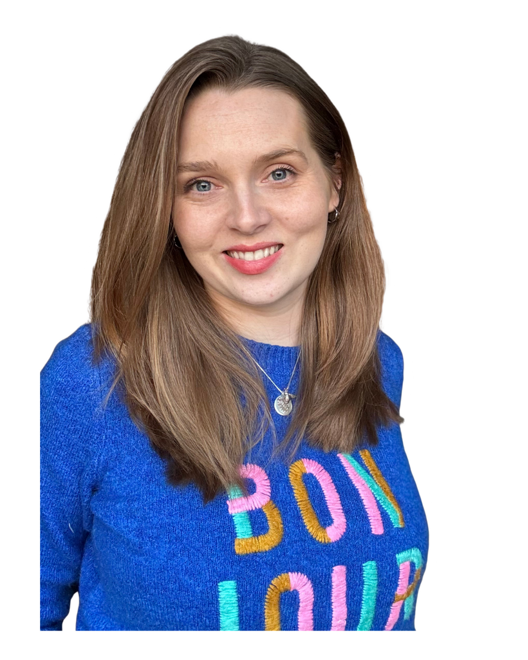 Young woman with long light brown hair, wearing a blue sweater with colorful embroidered text, silver necklace, and earrings, smiling.