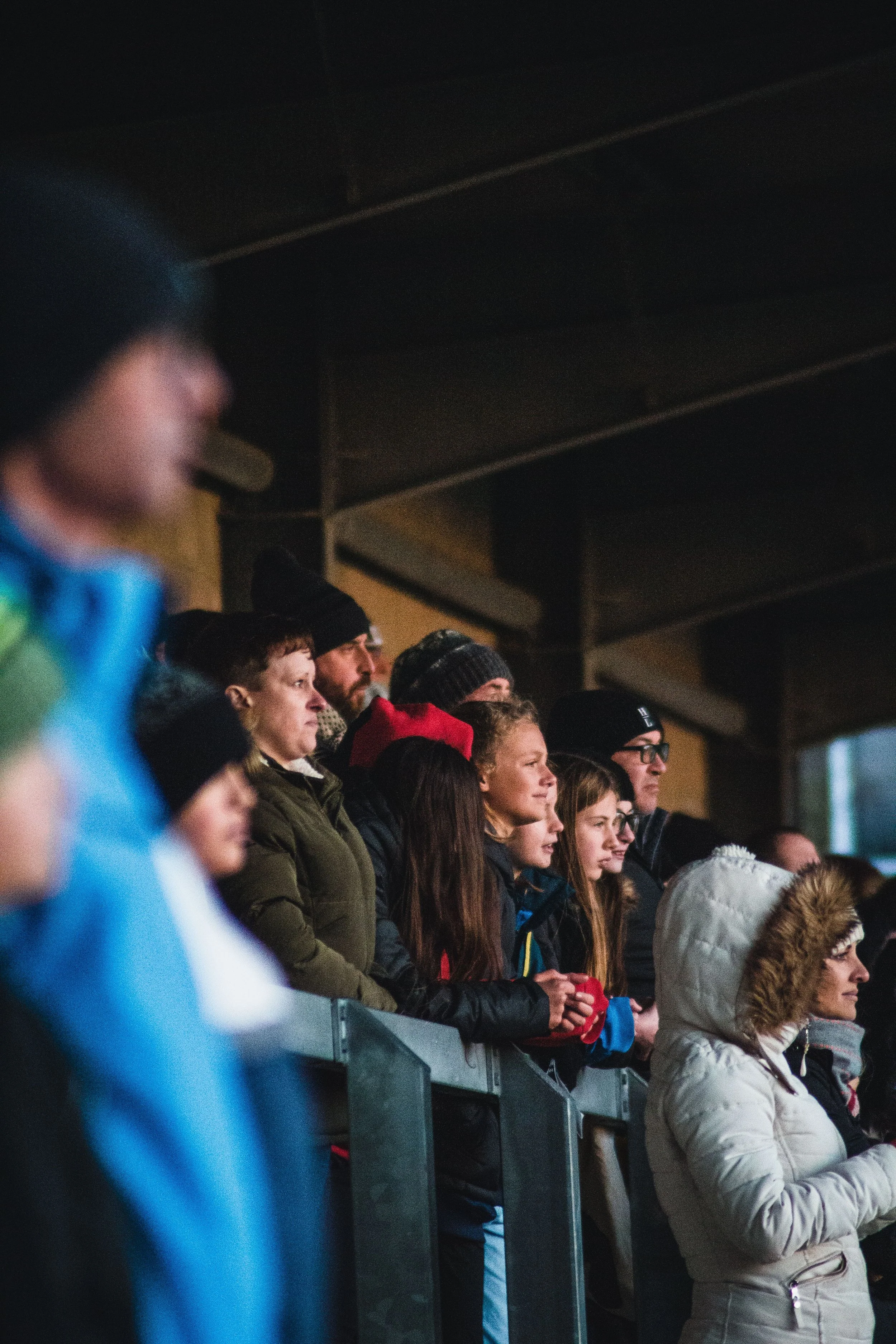 People standing and watching in an indoor venue, some wearing winter clothing like jackets and hats.