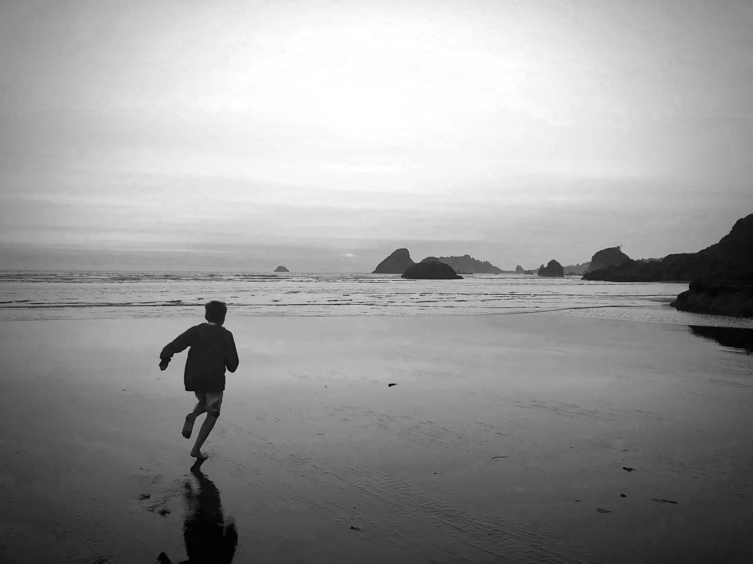 A person running on a beach at low tide, with rocky islands in the distance, black and white photograph.