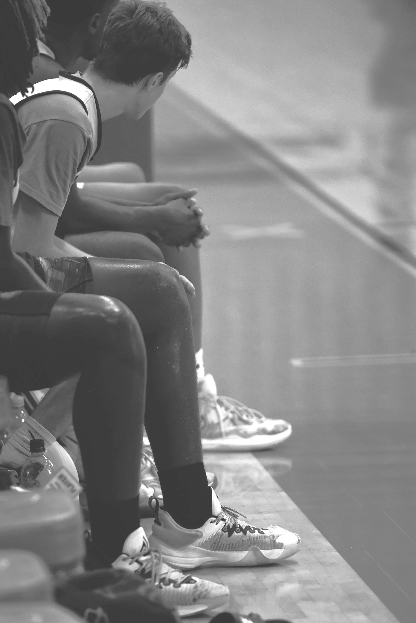 People sitting on a sports bench during a game, with sneakers and water bottles visible.
