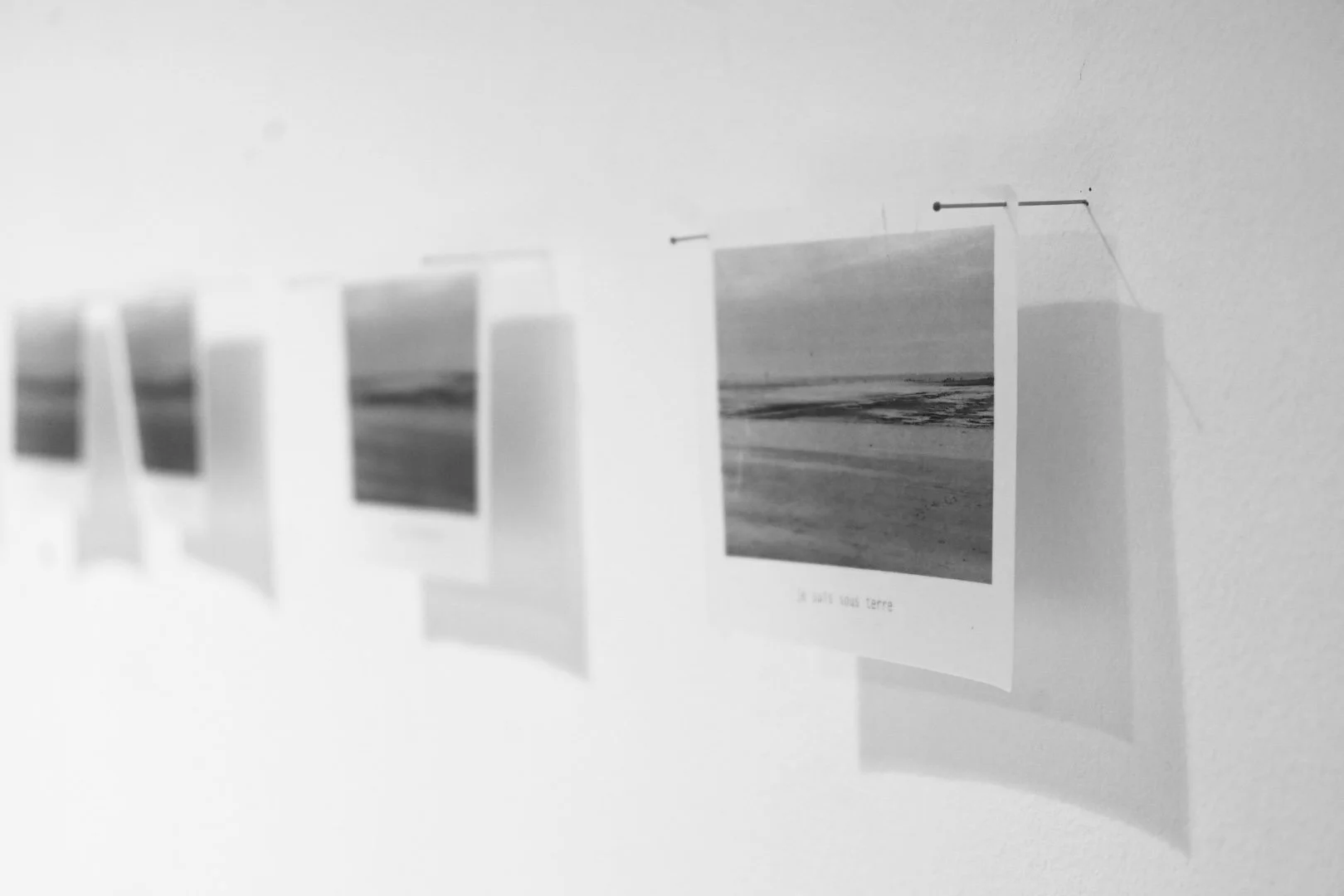 Photographies en noir et blanc de paysages de plage accrochées à un mur, suspendues par des épingles et un fil.